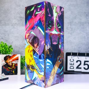 Op de afbeelding: Een rechthoekige houten lamp met levendige, veelkleurige stripboekillustraties van een personage met gloeiende ogen en intense uitdrukkingen. Het ontwerp bevat heldere roze, blauwe en gele tinten met zichtbare lasergesneden hoekverbindingen.