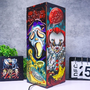 Puede incluir: Una lámpara rectangular de madera con ilustraciones de películas de terror. Un lado muestra una máscara de Ghostface, un teléfono de disco amarillo y el texto "do you like scary movies?". El otro lado muestra al payaso Pennywise con un globo rojo y "you'll float too".