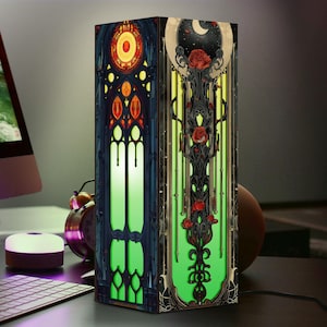 May include: A decorative lamp with a stained-glass design. One panel features a circular design with red and yellow accents, the other showcases roses and a crescent moon. The lamp is illuminated with a green glow, creating a striking visual.