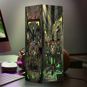 Puede incluir: Una lámpara rectangular que presenta una vibrante ilustración gráfica de varios paneles de un grupo de personajes jóvenes en un entorno urbano postapocalíptico. La obra muestra figuras detalladas, estructuras de piedra y acentos verdes brillantes.