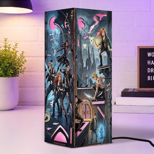 May include: A rectangular lamp featuring a vibrant, multi-character fantasy illustration set against a dark, gothic city backdrop. The artwork depicts several figures in dynamic poses, including individuals with weapons and glowing runes, illuminated by pink and blue light accents.