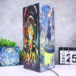 Może przedstawiać: Prostokątna drewniana lampa z wielowarstwowymi, wycinanymi laserowo panelami z żywymi ilustracjami fantasy. Jedna strona przedstawia dwie postacie w ciemnej hali, a druga postać stojącą na kamiennej platformie pośród błyskawic.