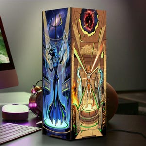 May include: A rectangular lamp featuring two distinct graphic panels. One side displays a blue-skinned figure in a flowing gown within a futuristic setting. The other side depicts two characters standing on a platform inside an ancient stone temple.