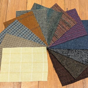 Op de afbeelding: Een verzameling van 12 stofstalen in verschillende patronen en kleuren, waaronder bruin, beige, grijs, blauw en paars. De stalen zijn in een cirkel op een houten oppervlak gerangschikt.