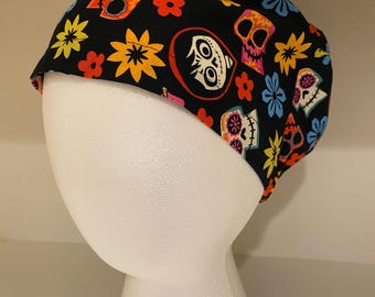 May include: A black skull cap featuring colorful sugar skull and floral patterns. The cap is adorned with orange, yellow, pink, and blue flowers, and various sugar skull designs. The cap is displayed on a white mannequin head.