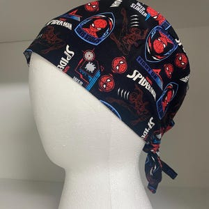 以下が含まれることがあります： スパイダーマンのデザインが施された黒色の手術用スクラブキャップ。キャップには、スパイダーマンのロゴ、アクションポーズ、および「Spider-Man」、「Web Slinger」、「Spider Sense」などのテキストがパターン化されています。キャップは後ろで結ばれています。