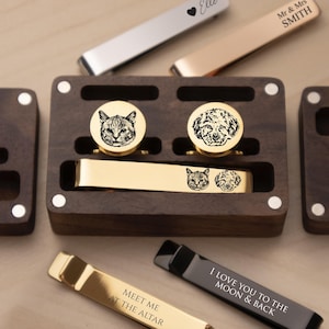 May include: A set of metal tie clips and cufflinks in a dark wood storage box. The gold tie clip features engraved cat and dog portraits. Other clips include text: Elle, Mr & Mrs SMITH, MEET ME AT THE ALTAR, and I LOVE YOU TO THE MOON & BACK.