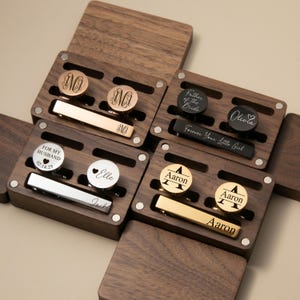 May include: A collection of personalized cufflinks and tie clips in wooden boxes. The cufflinks feature engraved initials, names, and dates. The tie clips are gold and silver-toned. Some boxes have text that reads "Father of the Bride" and "Forever Your Little Girl."