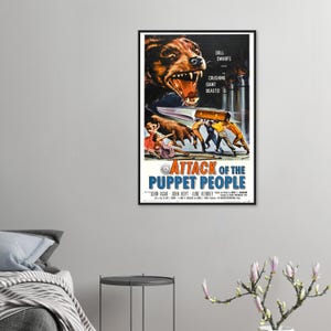 May include: A framed vintage movie poster for "Attack of the Puppet People." The poster features a menacing bear with bared teeth, a group of people, and the film's title in bold letters. The poster is in a black frame.