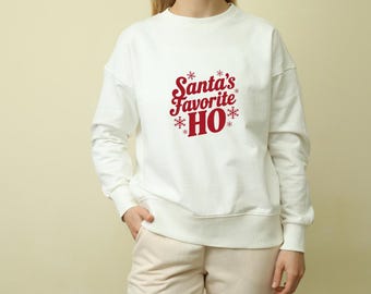 May include: White sweatshirt with the text "Santa's Favorite HO" in red script and snowflake accents. The long-sleeved crew neck top is a casual style, perfect for the holiday season.