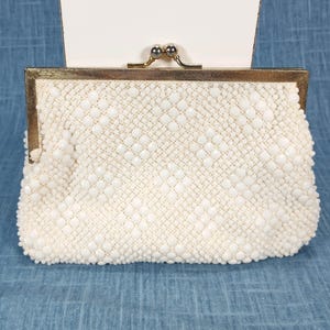 May include: Ivory beaded clutch with a gold-toned metal frame and clasp. The purse features a textured surface created by small, round beads. The clasp is a decorative element, adding to the vintage aesthetic of the bag.