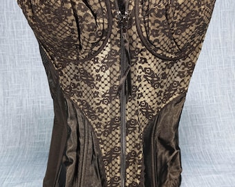 May include: Black and beige lace corset with a front zipper closure. The corset features a structured bodice with a delicate lace overlay and satin panels. White stitching accents the top edge.