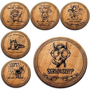 May include: A collection of six wooden coasters, each with a unique engraved design. The coasters feature animal illustrations and humorous quotes. They are round and made from light brown wood, perfect for drinks.