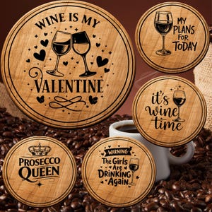 May include: A collection of round wooden coasters with various wine-themed designs. One coaster reads "Wine is my Valentine" with wine glasses and hearts. Other coasters say "My plans for today", "It's wine time", "Prosecco Queen", and "The Girls Are Drinking Again".