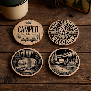 May include: Four round wooden coasters with camping-themed designs. One coaster reads "King of the Camper" with a camper illustration. Another says "Happy Campers Welcome" with a campfire graphic. The other two feature camper and nature scenes.