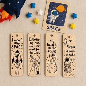 Puede incluir: Marcadores de libros de madera con temática espacial, con ilustraciones de cohetes, astronautas y planetas. Cada marcador tiene una cita diferente sobre el espacio. También hay un cohete de fieltro y decoraciones de estrellas.
