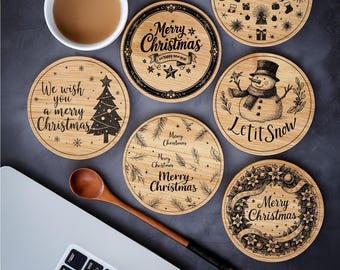 May include: A selection of round wooden Christmas coasters featuring festive designs and text, such as "Merry Christmas" and "Let it Snow." A cup of coffee, a wooden spoon, and a laptop are also visible.