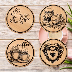 May include: Four round wooden coasters with black graphic designs. One coaster has the text "But First... Coffee" with a coffee cup illustration. Other coasters feature coffee cups, beans, and hearts.