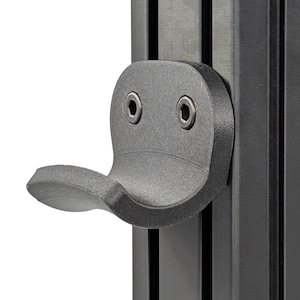 May include: A black plastic hook mounted to a black metal track. The hook has a rounded shape and is designed to hold objects.