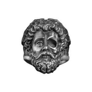 Könnte beinhalten: Ein silberner Ring mit detailliertem Design eines menschlichen Kopfes, der zur Hälfte aus einem Schädel besteht. Der Ring hat eine strukturierte Oberfläche mit aufwendigen Details in Haar und Bart, was eine einzigartige, gotische Ästhetik erzeugt.