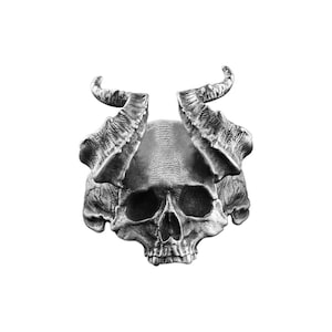 Op de afbeelding: Een zilverkleurige schedelring met grote, getextureerde hoorns. De schedel heeft gedetailleerde gelaatstrekken, waaronder oogkassen, een neusholte en een kaaklijn. De hoorns buigen omhoog en naar buiten.