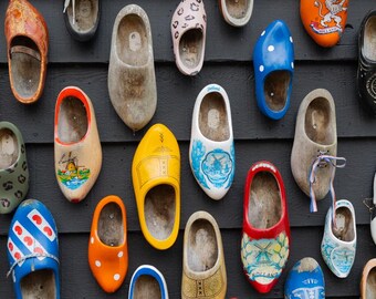 May include: A collection of colorful wooden clogs, or Dutch shoes, displayed on a dark wooden wall. The clogs vary in size and design, with painted details including windmills, polka dots, and floral patterns.