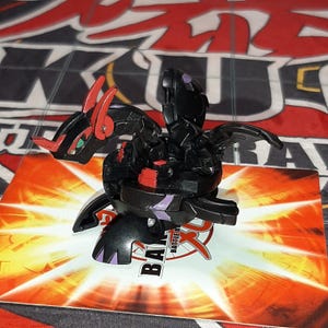 May include: A black and red toy dragon figure with purple detailing. The dragon is positioned on a card with the word "Battle" visible. The background is a red and black patterned surface.