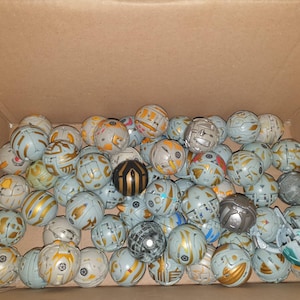 May include: A box filled with a variety of gray and gold toy balls. The balls have different designs and patterns.