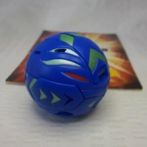 May include: A blue spherical toy with green and silver accents. The toy has a geometric design with arrow-shaped details. A colorful card is in the background.