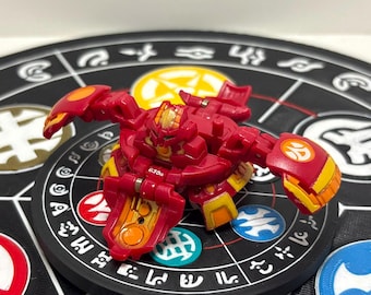 Könnte beinhalten: Eine rote und gelbe Bakugan-Spielfigur mit mechanischen Merkmalen und beweglichen Gliedmaßen, die den Text 630G auf ihrem zentralen Körper zeigt. Die Figur hat ein komplexes, segmentiertes Design mit orangefarbenen Akzenten und einem Symbol.
