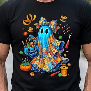 May include: A black t-shirt featuring a graphic of a blue ghost wearing a large floral bow. The ghost holds a blue pumpkin basket filled with thread spools. Surrounding the ghost are sewing supplies including needles, buttons, and spools of thread.