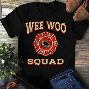 Peut inclure: T-shirt noir avec un emblème de pompier rouge et or et le texte "Wee Woo Squad" dans un motif à carreaux or et noir.