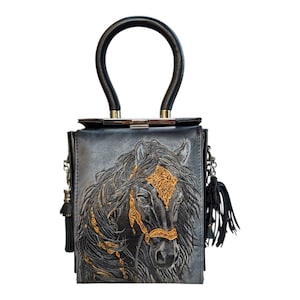 May include: A square, gray leather handbag with a black handle and a detailed embossed horse head design. The horse has gold-colored accents on its bridle and mane. The bag features a silver clasp and black tassels.