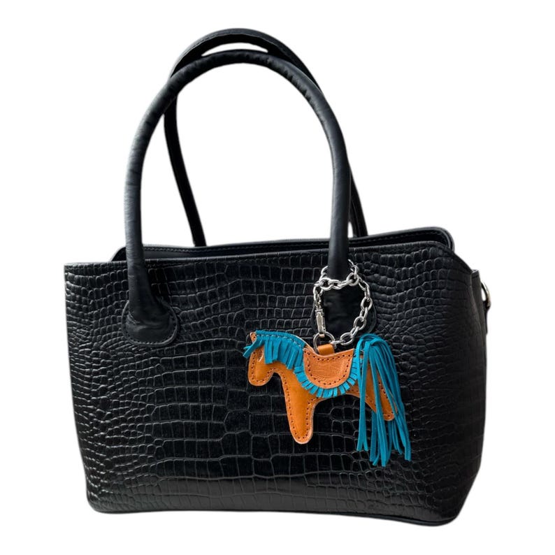 May include: Black leather tote bag with a crocodile embossed pattern. The bag has two top handles and a small orange and blue leather horse charm attached to a silver chain.