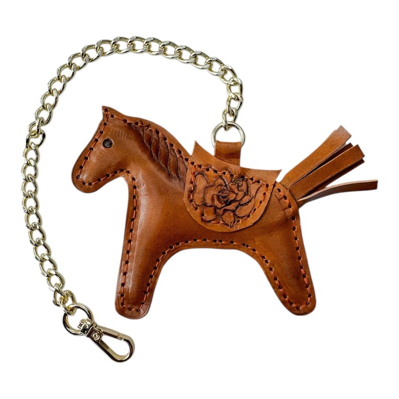 May include: A brown leather horse keyring with a gold chain. The horse has a saddle with a floral design and a fringe tail.