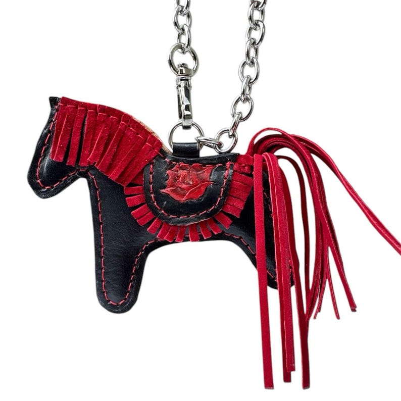 May include: A black leather horse charm with red fringe detail. The charm is attached to a silver chain.