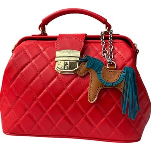 Puede incluir: Un bolso de m&eacute;dico acolchado rojo con un cierre dorado y un dije de caballo marr&oacute;n con una crin y cola turquesa.