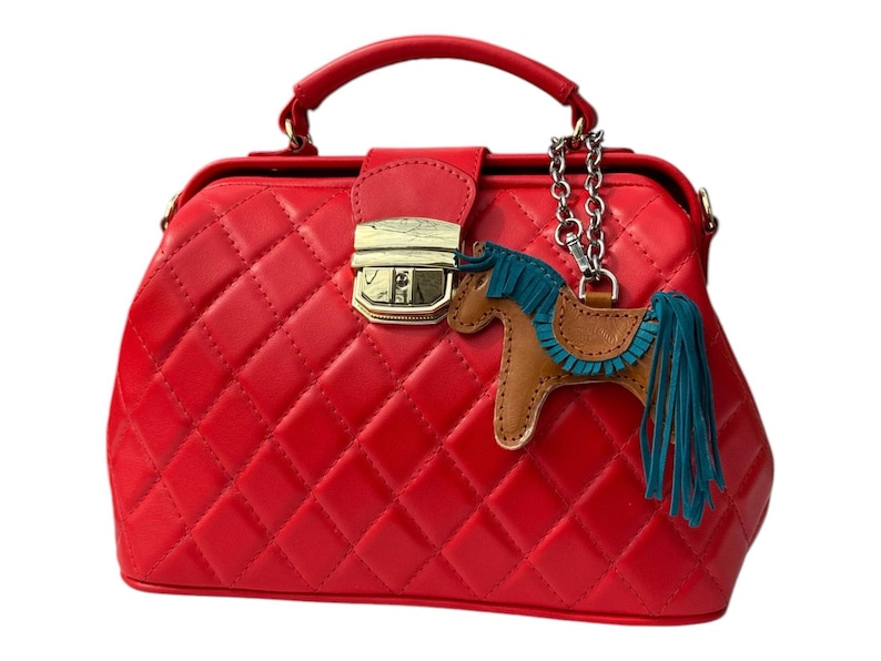 Puede incluir: Un bolso de m&eacute;dico acolchado rojo con un cierre dorado y un dije de caballo marr&oacute;n con una crin y cola turquesa.
