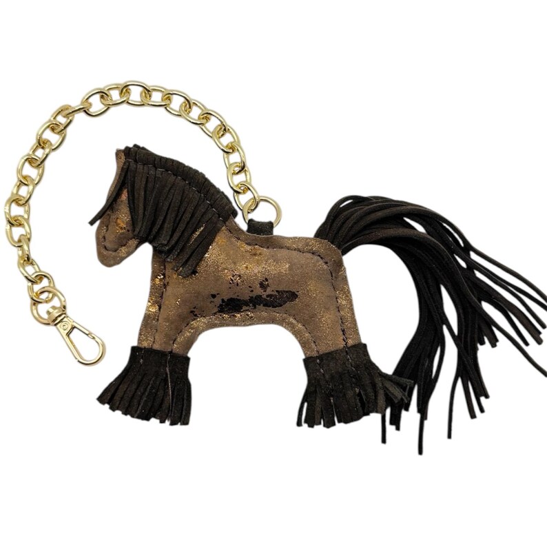 Op de afbeelding: Een bruin en goud paardvormige sleutelhanger met een gouden ketting en sluiting. Het paard heeft zwarte franjes voor de manen, staart en benen. Het lichaam van het paard heeft een distressed gouden metallic afwerking.