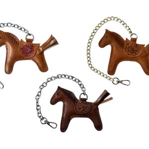 May include: Three brown leather horse keychains with silver and gold chains. Each horse has a saddle with a floral design.