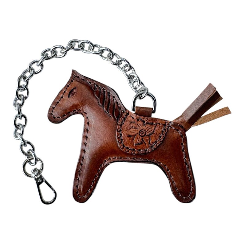 May include: A brown leather horse keyring with a silver chain. The horse has a saddle with a floral design and a tail with a fringe.