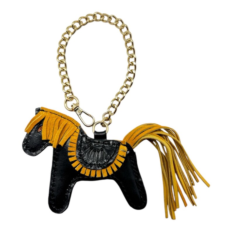 May include: A black leather horse keychain with a gold chain and yellow fringe. The horse has a saddle and a tail made of yellow fringe.