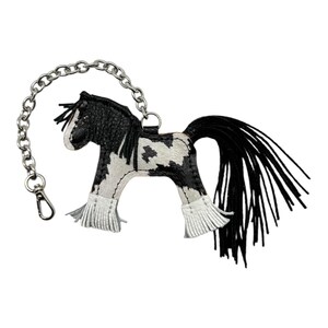 Op de afbeelding: Een zwart-witte leren paarden sleutelhanger met een zilveren ketting en sluiting. Het paard heeft een zwarte manen en staart, en witte franjes op de benen. Het ontwerp is ge&iuml;nspireerd op het Gypsy Vanner paard.