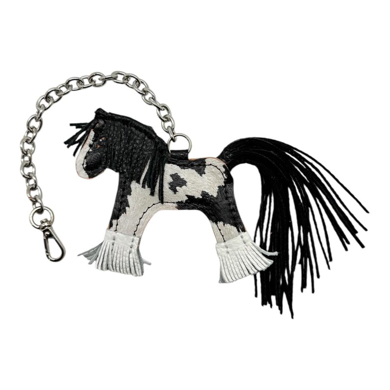 Op de afbeelding: Een zwart-witte leren paarden sleutelhanger met een zilveren ketting en sluiting. Het paard heeft een zwarte manen en staart, en witte franjes op de benen. Het ontwerp is ge&iuml;nspireerd op het Gypsy Vanner paard.