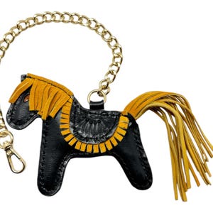 Puede incluir: Llavero de cuero negro en forma de caballo con una cadena dorada y detalles de flecos amarillos.