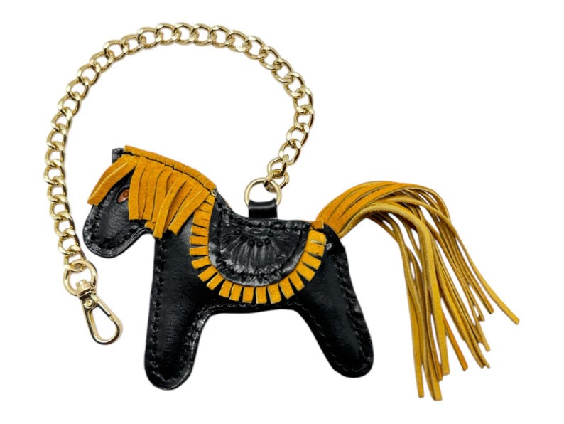 Puede incluir: Llavero de cuero negro en forma de caballo con una cadena dorada y detalles de flecos amarillos.