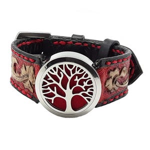 Pode incluir: Uma pulseira de couro preta e vermelha com um difusor de aromaterapia prateado. O difusor apresenta um design de árvore da vida. A pulseira tem costuras vermelhas e padrões florais em relevo.