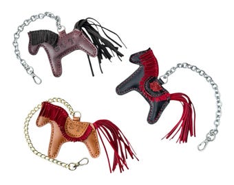 May include: Three leather horse keychains with silver chains. The horses are brown, black, and tan with red fringe. The horses have the letters "ST" embossed on them.