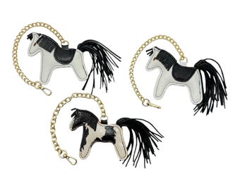 May include: Three leather horse keychains. Each keychain features a black and white horse design with a black mane and tail. The keychains are attached to a gold-colored chain with a clasp.