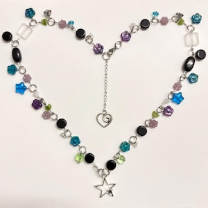 May include: A heart-shaped necklace with a silver chain, adorned with black, blue, purple, and green beads. It features a heart pendant and a star pendant. The beads are of different shapes and sizes, creating a unique design.
